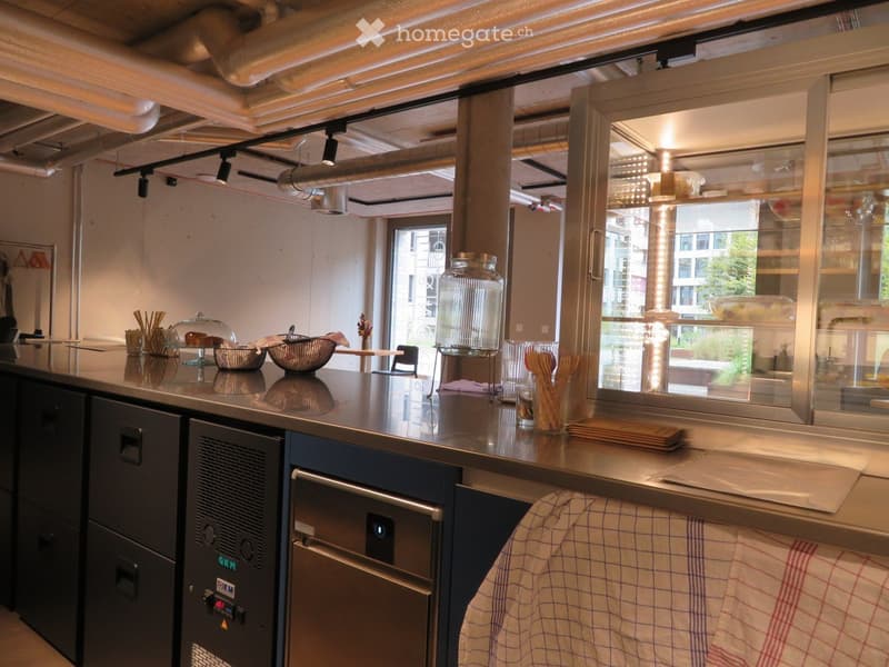 modern kitchen with stainless steel countertops, various kitchen utensils, cabinet drawers, a dishwasher, a large glass door with shelves, and a hanging rack.