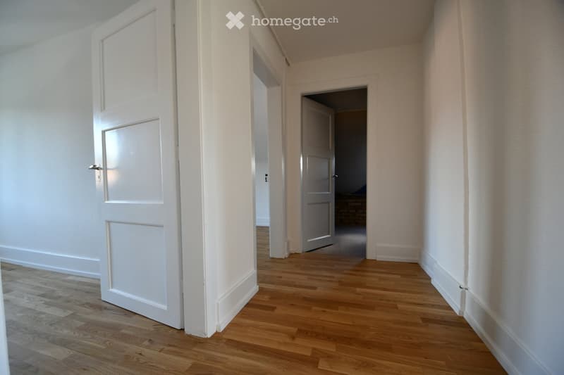 Empty hallway with wooden floors, white walls, two doors.