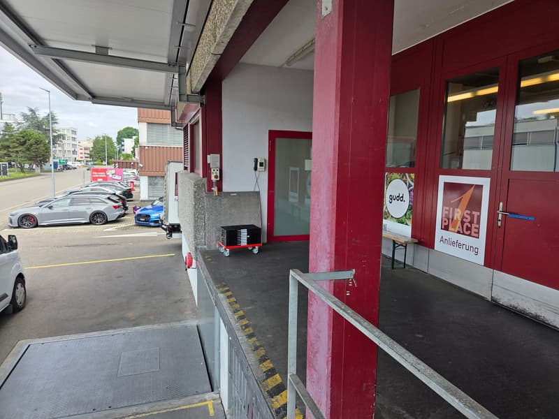 Parking space outside a building, vehicles parked, benches, red pillars, building entrance, streetlight