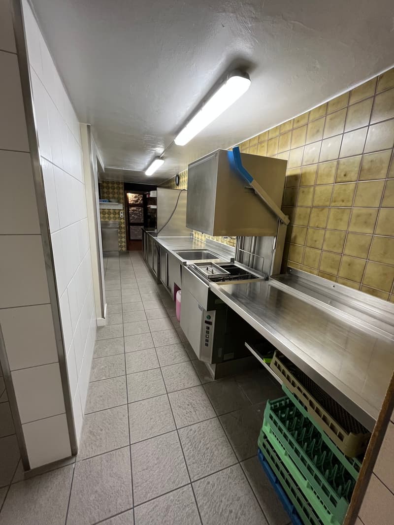 Commercial kitchen with stainless steel appliances, countertops, and tile flooring. Includes a washing machine and dishwasher.