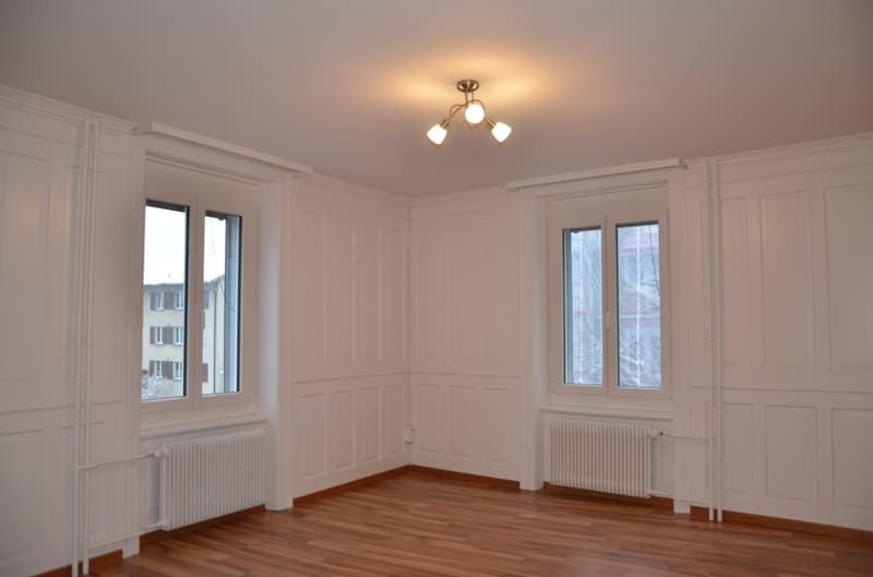 empty room, white walls, wooden floor, two windows, radiators, ceiling lamp