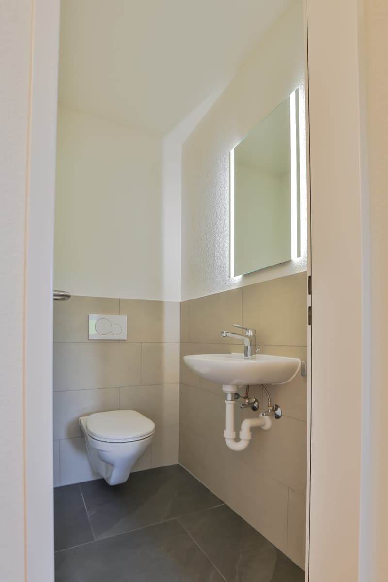 small white bathroom with white toilet, white sink, mirror, white floor, and tiled wall