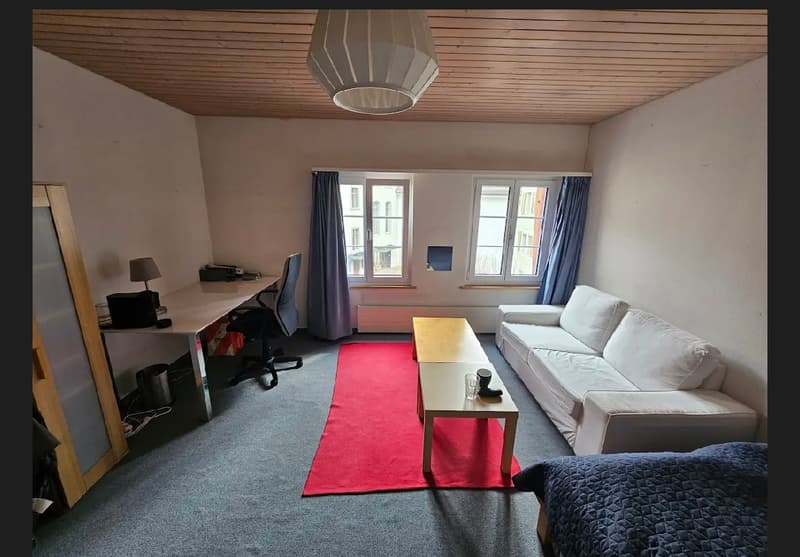 Carpeted room, white couch, white desk, red carpet, table, lamps, radiator, chair, trash can, cabinet, windows with curtains, door
