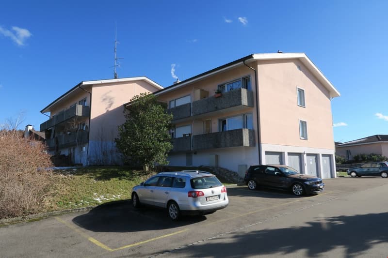 3-story apartment building with beige exterior, balconies, and a parking lot in front