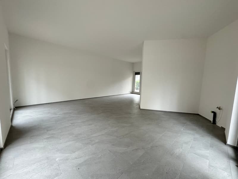 Empty room with white walls, gray tiled floor, and a glass door leading to a small outdoor area.