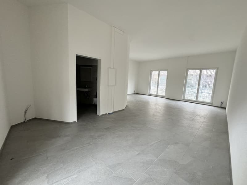 Empty room with white walls, gray tiled floor, two glass doors, and an open door leading to a bathroom.