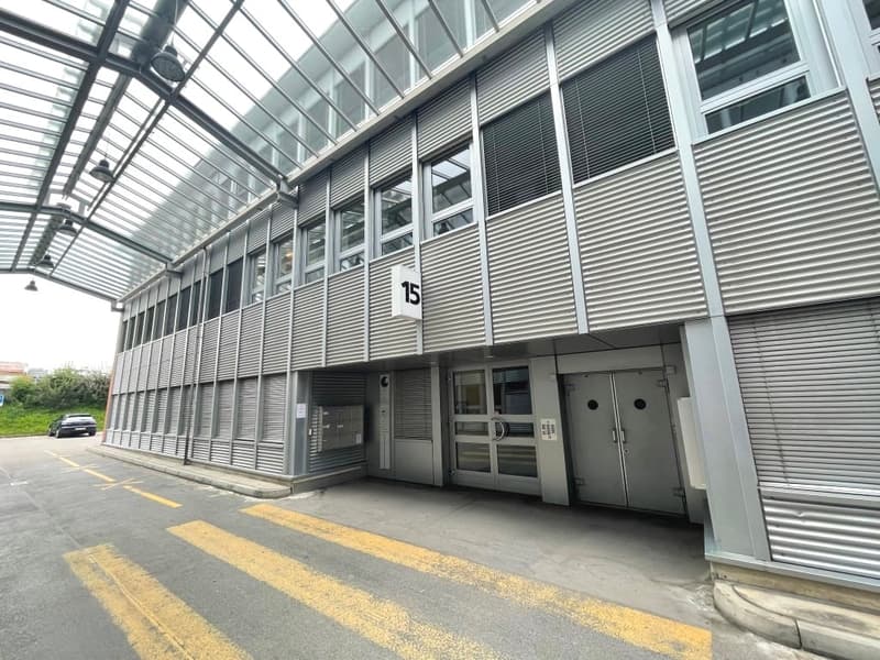 A modern, multi-story commercial building with a glass and metal facade. The building has a numbered entrance and appears to have parking spaces in front of it.