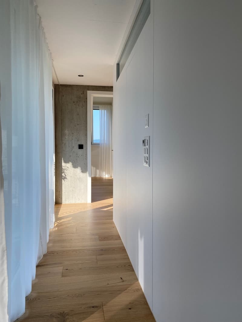 wooden floor, white walls, white curtains, concrete wall, open door, window with white curtains