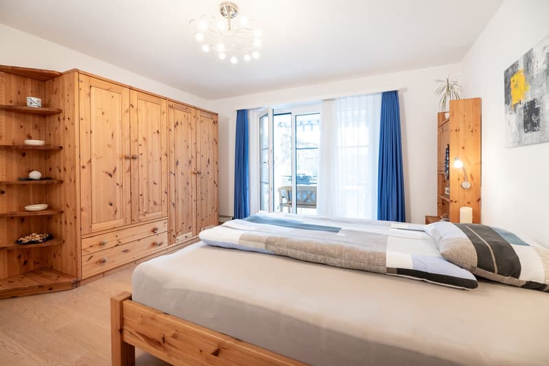 wooden bed, wooden wardrobe, wooden shelves, chandelier, double doors leading to balcony, white walls, white floor