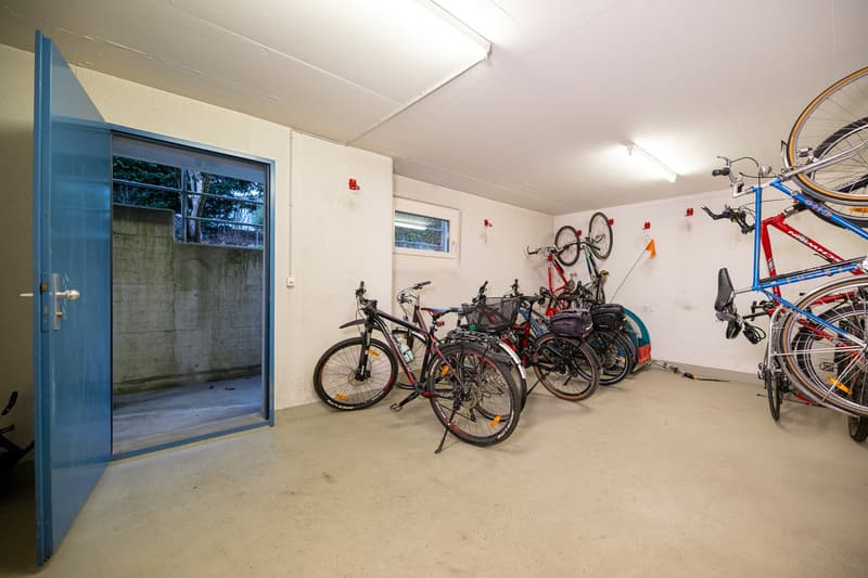 A room with several bicycles parked on the wall and floor, a blue door, and a white wall.