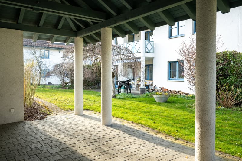 covered walkway, brick floor, green lawn, trees, shrubs, plants, grill, chairs, table
