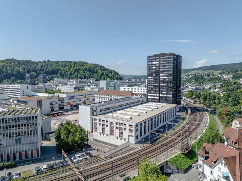 industrial building with solar panels, modern office building, older architectural style buildings, train tracks, parked cars, greenery