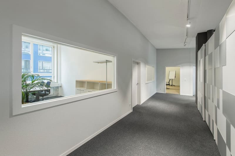 hallway with carpeted floor, white walls, glass window, white shelves, black chair, desk, potted plant, ceiling light