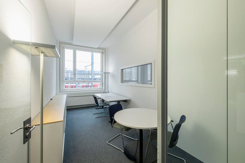 empty room, white walls, gray floor, round white table, white tables against the wall, chairs, large window