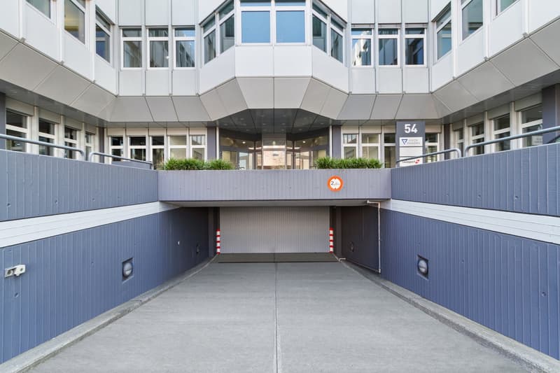 Modern building with many windows, entrance way with metal railings, garage entrance with sign 54