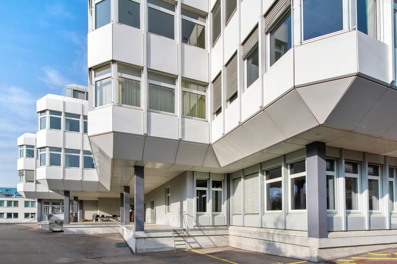 modern office building, white exterior, large windows, multiple floors, concrete base, entrance with stairs