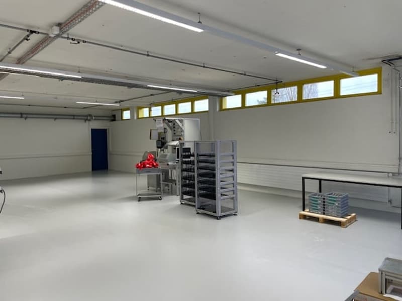 Large open space with high ceilings, concrete floor, storage racks and equipment, and windows along the upper walls.
