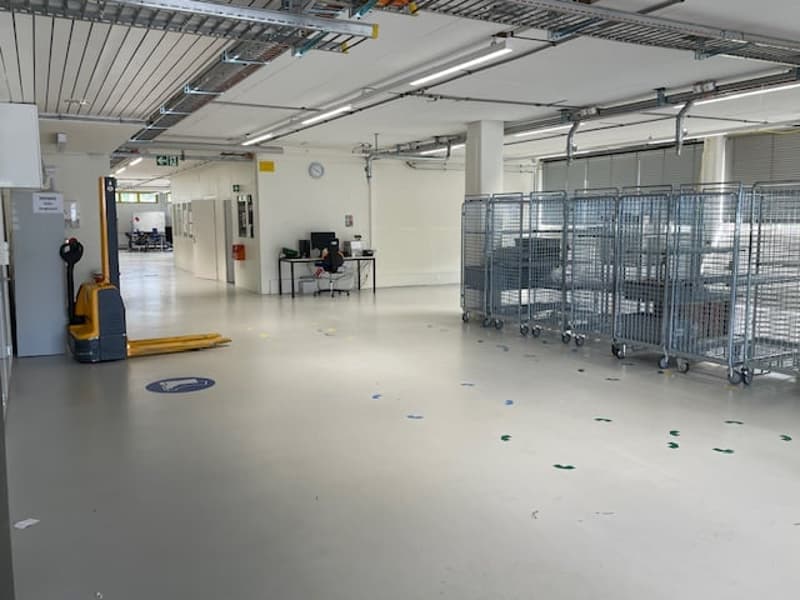 Large open space with concrete flooring, metal shelving units, and a forklift visible. The space appears to be a warehouse or storage facility.