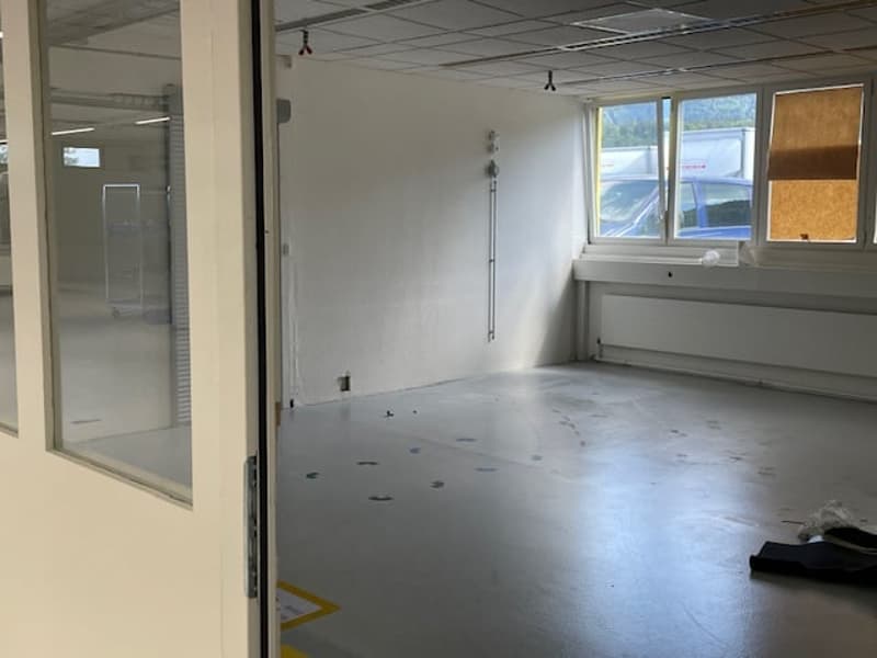 The image shows an empty office space with white walls, a concrete floor, and a glass partition wall. The room appears to be in a state of renovation or preparation for a new tenant, with some construction materials visible on the floor.