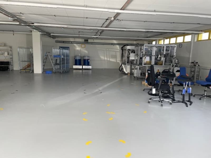 Large open space with concrete floor, metal shelving units, and various equipment and tools. The space appears to be used for storage or industrial purposes.