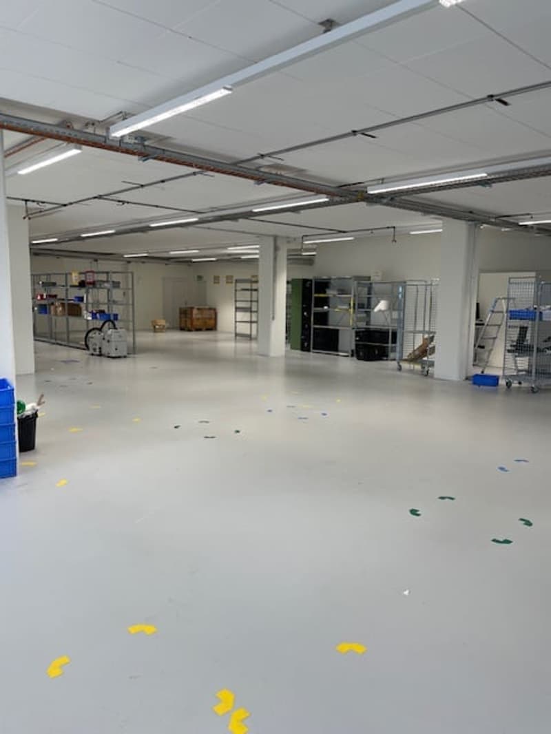 Large open warehouse space with concrete flooring, shelving units, and various equipment and supplies visible.