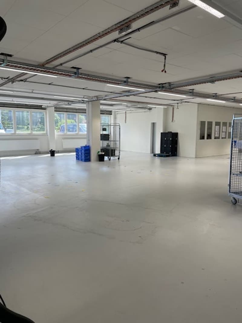 Large open space with concrete floor, overhead lighting, and storage shelves and containers