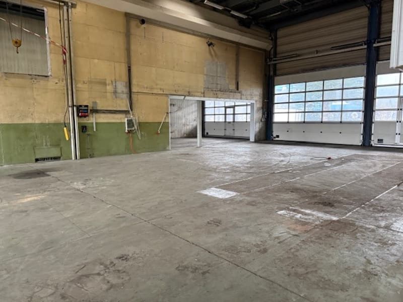 Empty warehouse with concrete floor, green and beige walls, large white doors, no equipment visible