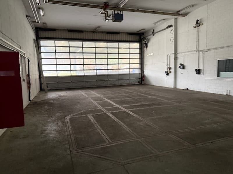 A large open garage with a large glass door, high ceilings, and a concrete floor