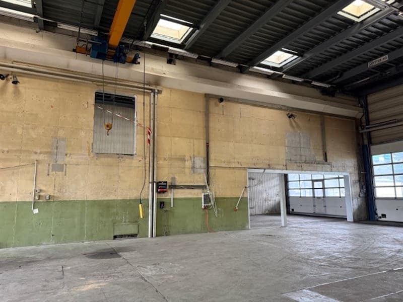 Empty warehouse with concrete floor, brick walls, yellow door, metal structures, wires, security cameras.