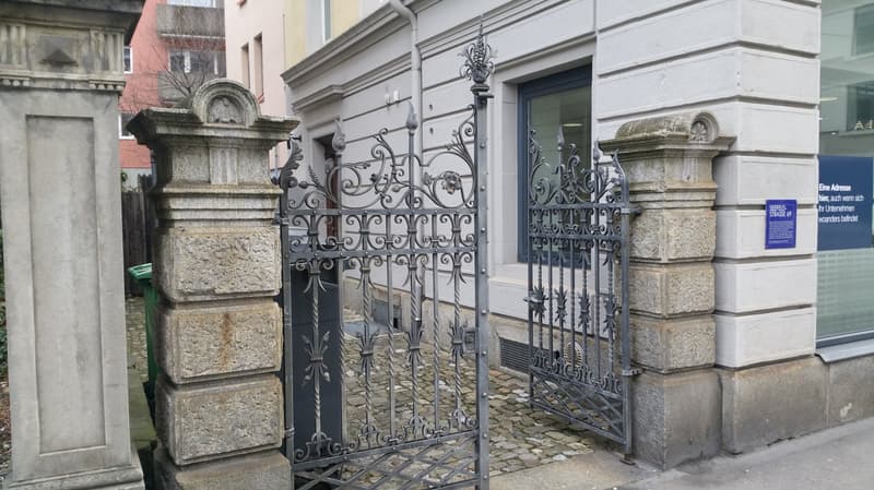 Wrought iron gate, stone columns, paved cobblestone road
