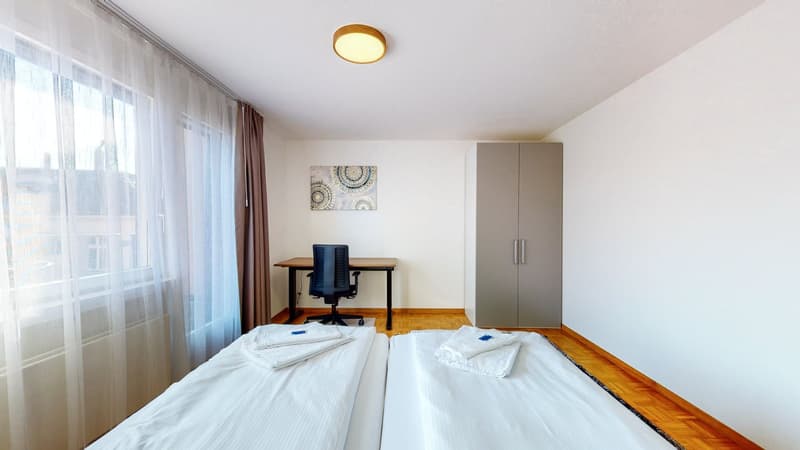 two single beds, desk, chair, grey wardrobe, white curtain, picture, wooden floor