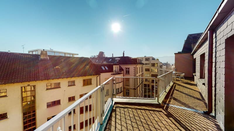 Sunlit balcony, metal railings, tiled floor, multiple buildings, city view