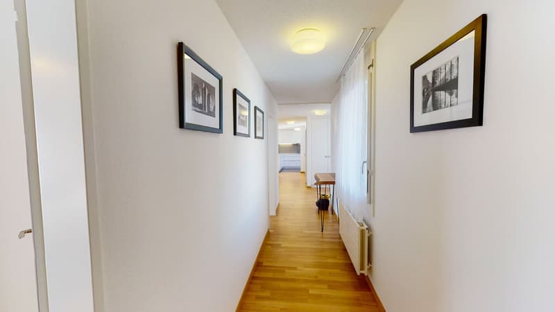 Empty hallway with white walls, wooden floor, and framed black-and-white pictures on the wall.