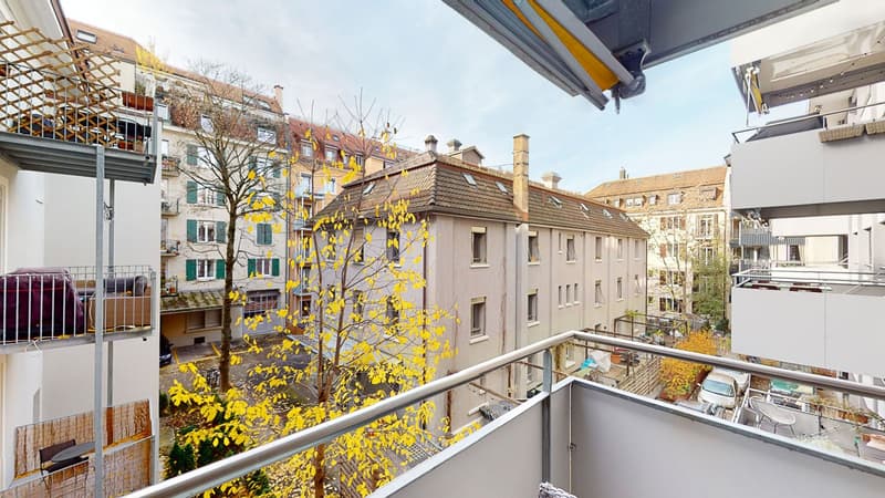 Balcony with metal railings, with trees in the background, and another building with balconies visible in front.