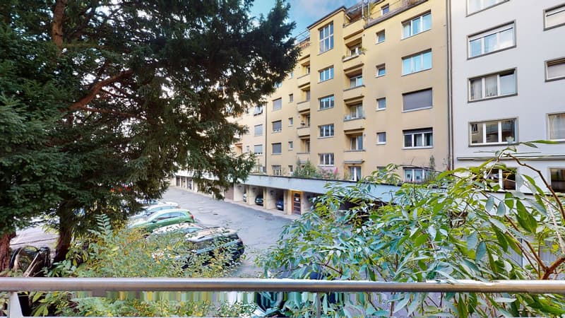 Apartment building, yellow and white exterior, several car parked, large tree, metal railing