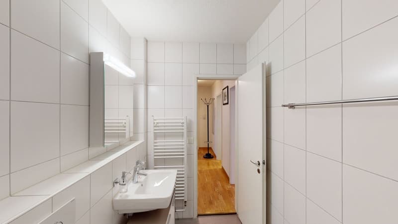White tiled walls, mirror, wooden floor, sink, and faucet