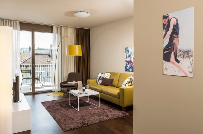 open layout, yellow sofa, glass table, yellow floor lamp, brown carpet, sliding doors to balcony, modern decor
