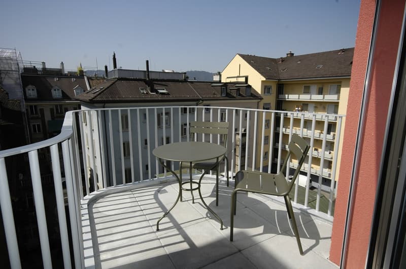 Small balcony with a round table and chairs, metal railing, tiled floor, city view