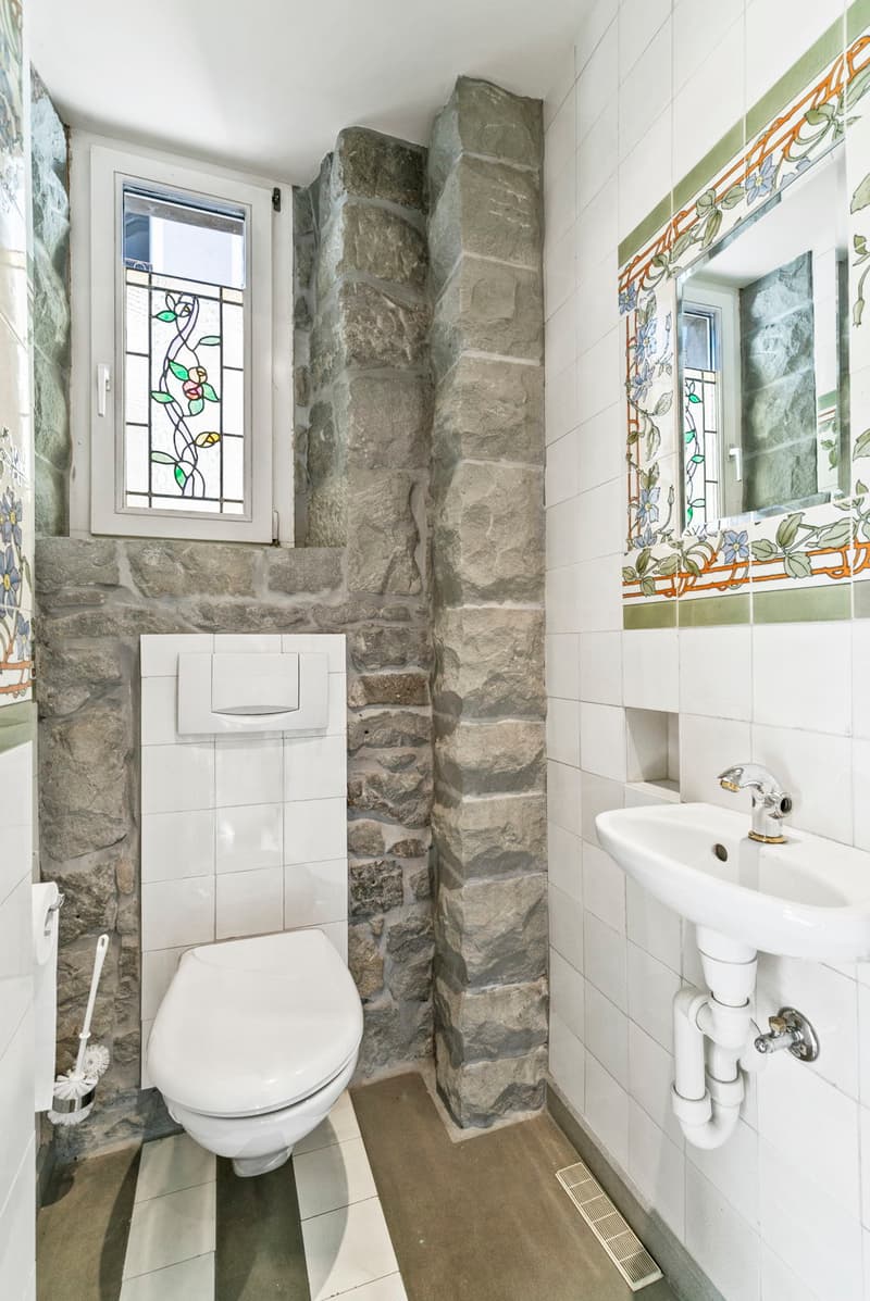 Bathroom with stone walls, stained glass window, toilet, sink, and tiled floor.