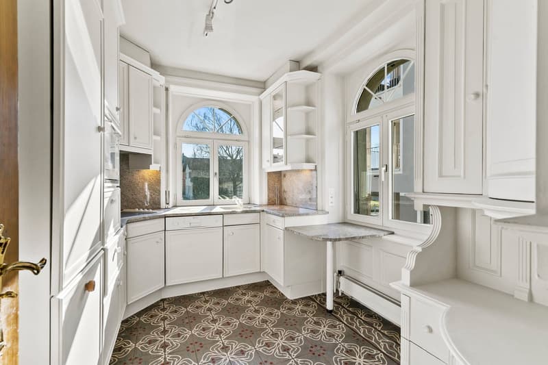 Spacious kitchen with white cabinetry, granite countertops, arched window, and patterned tile flooring