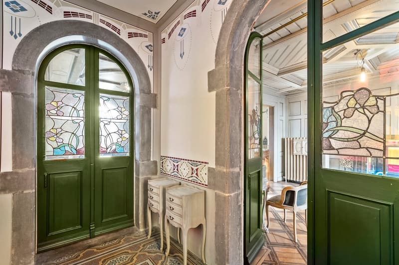 Ornate arched doorway with stained glass windows, green wooden doors, antique dresser, tiled floor, decorative wall patterns