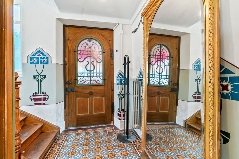 Ornate wooden doors with stained glass windows, decorative tiled floor, fireplace, and ornate gold-framed mirror on the wall