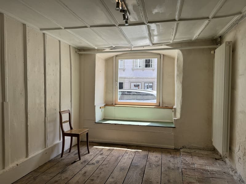 Empty room with wooden floor, white walls, wooden chair, bench seating by the window, ceiling lamp