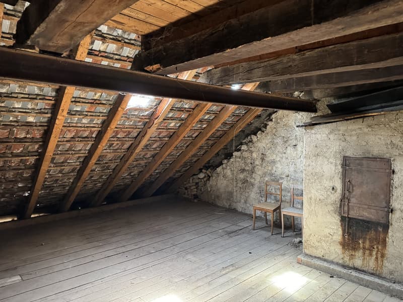 empty attic room, wooden beams, wooden floor, two wooden chairs, brick wall, and rusted door