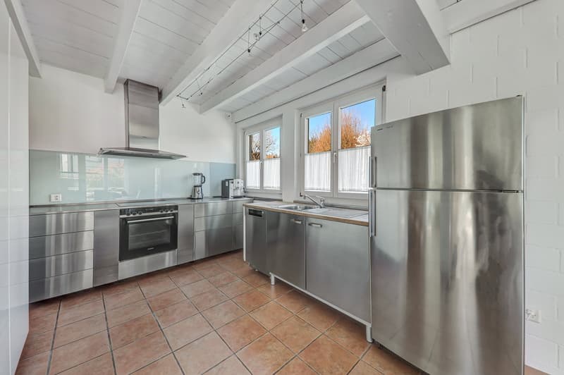 Spacious kitchen with stainless steel appliances, including a refrigerator, oven, and dishwasher. The kitchen has a tiled floor and large windows providing natural light. The cabinets and countertops are made of stainless steel, creating a modern and slee