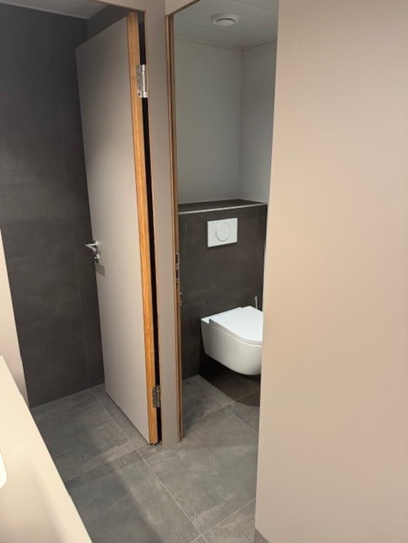 Bathroom with toilet, open door, tiled floor, mirror, white toilet, gray walls