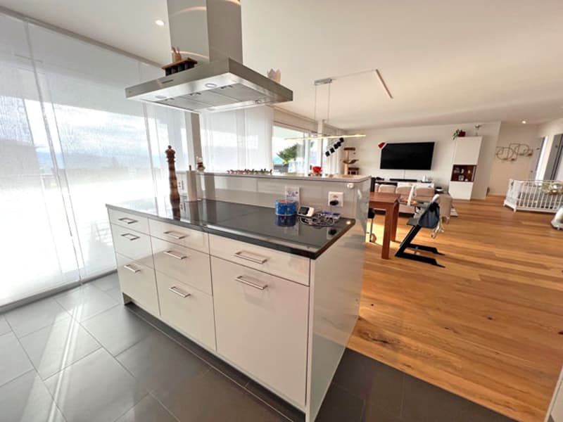 Modern kitchen with large island, white cabinetry, black granite countertop, stainless steel range hood, open to living area with dining table