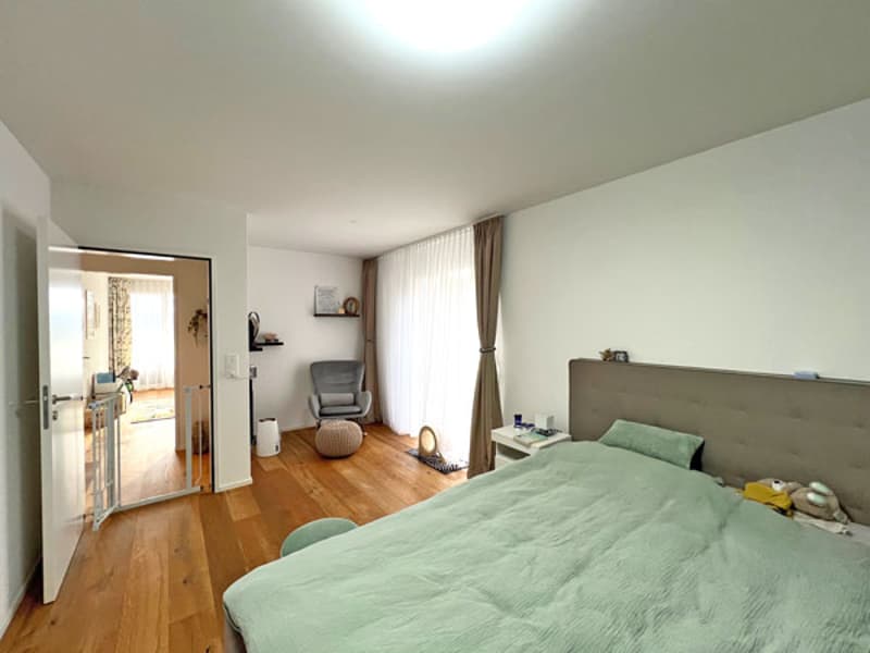 modern bedroom with bed, bedside tables, gray armchair, white doors, wooden floor, curtains