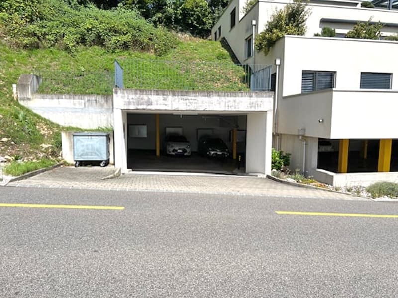 Garage building with two cars parked inside, located on the side of a sloped area