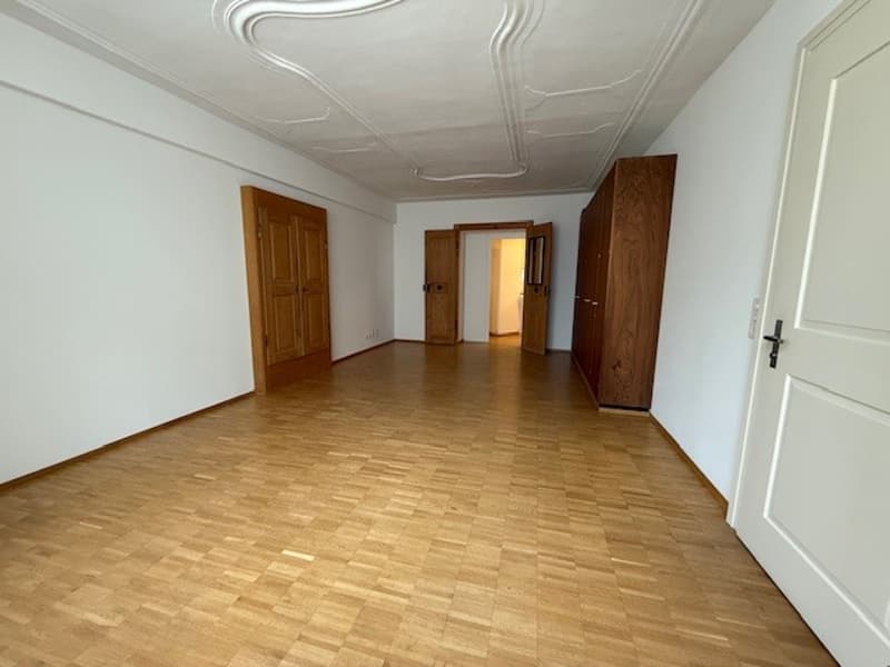 empty room with wooden floors, two doors, white walls, wooden cupboard